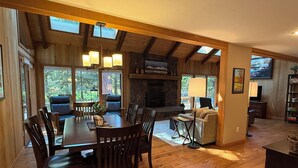 A spacious living area with a wooden dining table, chairs, a fireplace, and a stone wall. - 3-bedroom mountain oasis in Black Butte Ranch surrounded by trees (Sisters)