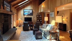 A spacious living room with a fireplace, a television, and a cozy seating area. - 3-bedroom mountain oasis in Black Butte Ranch surrounded by trees (Sisters)