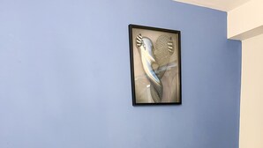Et soveværelse med en knapbetrukken sengegavl, en seng med hvide sengetæpper, et natbord med en lampe og et indrammet kunstværk på væggen.
