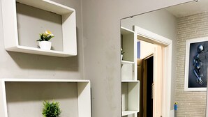 Et badeværelse med en hvid vask, to hvide hylder med planter, og et spejl der viser en dør og en væg med et struktureret mønster.