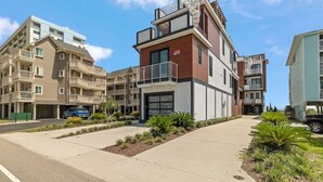 A modern multi-story residential building with balconies, a garage, and a well-maintained landscaped area. - Carolina Skies - Rooftop Deck - Ocean Views (Carolina Beach)