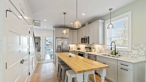 A modern kitchen with a central island, pendant lights, and a view of the beach through the window. - Carolina Skies - Rooftop Deck - Ocean Views (Carolina Beach)