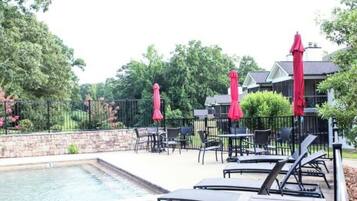 A poolside area with lounge chairs and red umbrellas, surrounded by a stone wall and greenery.