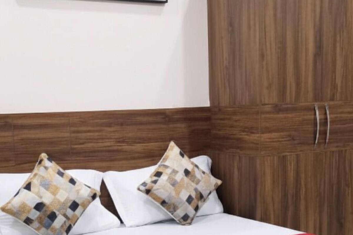 A neatly made bed with a red runner, two patterned pillows, and a wooden headboard.