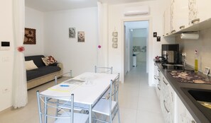 A compact living space with a dining area, kitchenette, and a sofa with patterned cushions. - Domu S'Aratzia - 2km from the sea - with private parking (Quartu Sant'Elena)