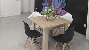 Un espace repas avec une table en bois, des chaises noires et une fresque murale.