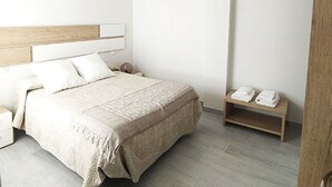 Une chambre à coucher moderne avec un lit, des tables de chevet et un petit banc en bois.