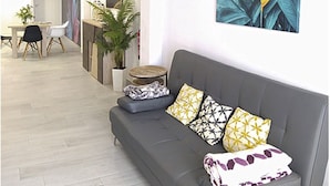 Un salon moderne avec un canapé gris, des coussins à motifs et une grande estampe représentant des plantes accrochée au mur.