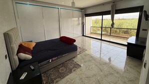 A bedroom with a bed, a desk, and a large window with a view of greenery.