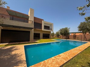 Una casa moderna de dos pisos con piscina, un patio cubierto y un garaje.