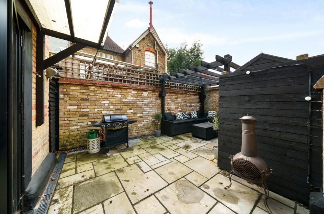 A patio area with a brick wall, a grill, a black outdoor sofa, and a wood-burning stove.