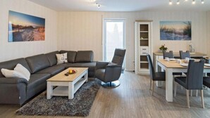 A modern living room with a grey sofa, a coffee table, and a dining area with a table and chairs. - Tillmanns Stadtlounge Exclusive 5 star vacation apartment in Norden. (Norden)