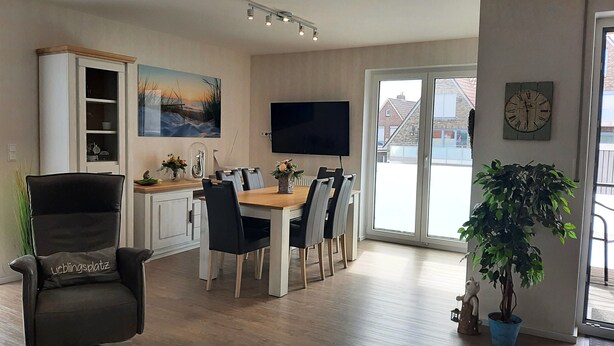 A modern living room with a dining area, a flat-screen TV mounted on the wall, and a large window providing a view of the outside. - Tillmanns Stadtlounge Exclusive 5 star vacation apartment in Norden. (Norden)