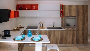 A modern kitchen with white cabinets, a wooden backsplash, a built-in oven, and a dining area with a white table and chairs. - Castellinaria Holiday (Castellana Grotte)
