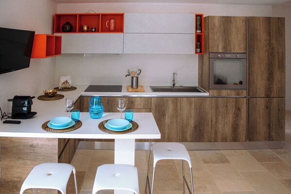 A modern kitchen with white cabinets, a wooden backsplash, a built-in oven, and a dining area with a white table and chairs.