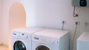 Een wasserijruimte met twee Bosch wasmachines, een kunstwerk van een cactus aan de muur, en een digitale klok.