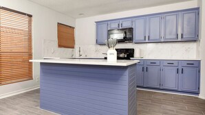 Una cocina con una isla central, armarios azules, microondas y una estación para café.