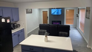 Una cocina moderna con refrigerador, cafetera y comedor con una mesa y sillas blancas.