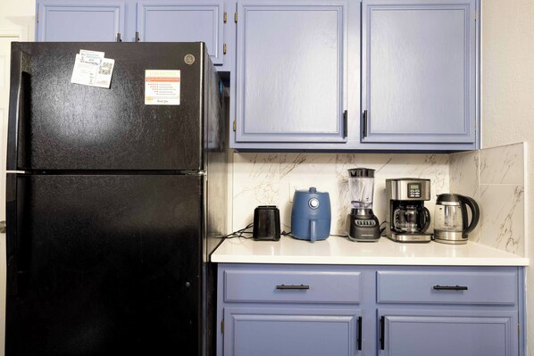 A kitchen with a black refrigerator, a coffee maker, a blender, and a kettle on the counter.