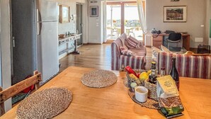 Een ruime keuken met houten balken, een zithoek met een gestreepte bank, en uitzicht door de open deur.