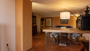 A dining area with a wooden table and chairs, a hanging lamp, and a kitchen area with a stove and cabinets. - Villa VILLACOLLE - Marsala (Marsala)