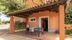 A covered patio with a table and chairs, a tiled floor, and a building with orange walls and a tiled roof. - Villa VILLACOLLE - Marsala (Marsala)
