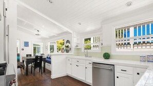 Una cocina con muebles blancos, lavavajillas y una zona de comedor con mesa y sillas.