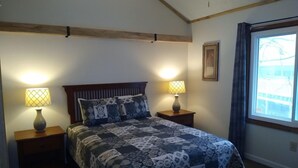 A bedroom with a bed, two bedside lamps, a window, and a framed picture on the wall.