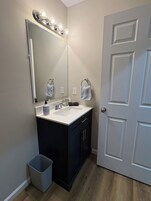 A bathroom with a vanity, sink, mirror, and a door.