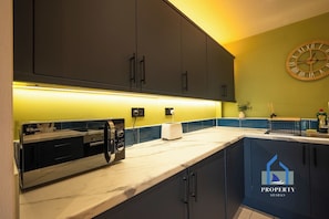 Una cocina moderna con armarios oscuros, encimera de mármol, horno empotrado y un reloj de pared.