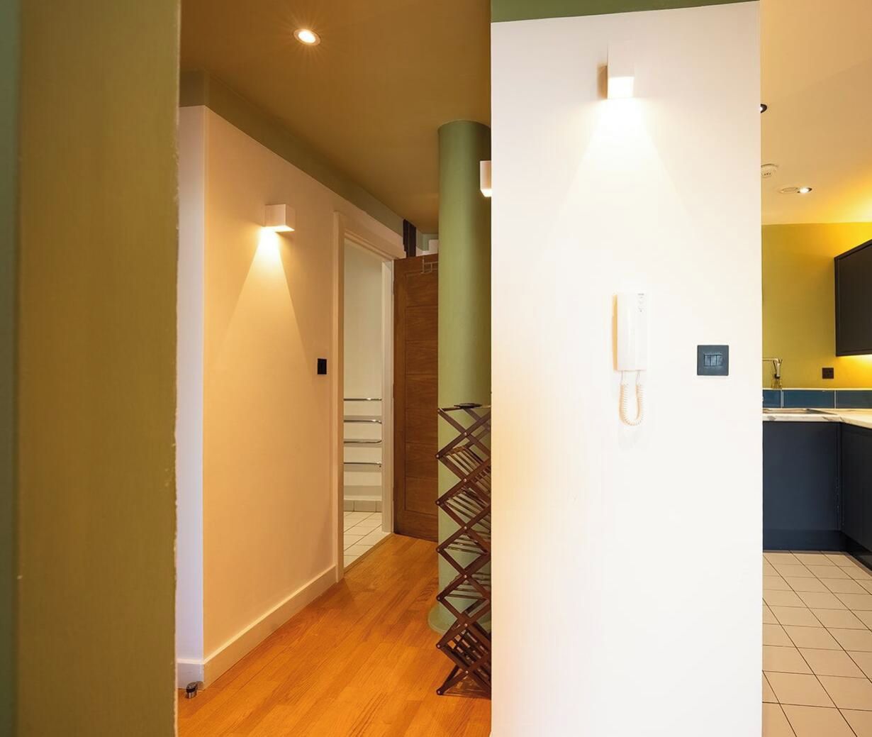 A hallway with a wooden floor, a white door, and a wall-mounted telephone.