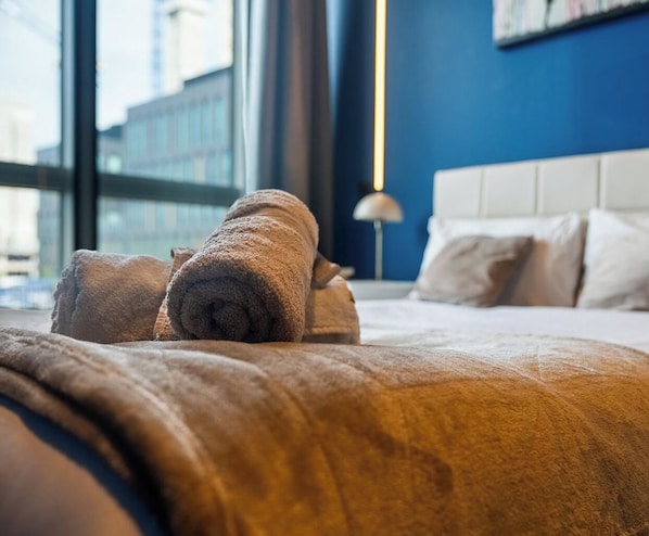 Una cama bien hecha con toallas enrolladas y un cabecero blanco en una habitación de hotel.
