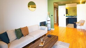 Una sala de estar con sofá, una mesa de centro y una estantería. Se ve una cocina al fondo.