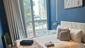 Ett modernt hotellrum med en stor säng, utsikt över staden genom stora fönster som sträcker sig från golv till tak, och en blå accentvägg.