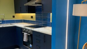 Ett modernt kök med en inbyggd ugn, en mikrovågsugn och en spis. Det finns en diskho med blandare och en bänkskiva med en köksfläkt ovanför. Köket har blå skåp och en vit väggbeklädnad bakom bänkskivan.