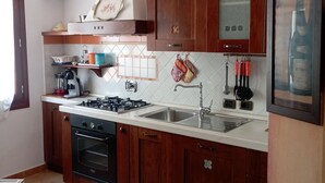 Une cuisine avec des meubles de rangement en bois, une cuisinière à gaz, un évier et un dosseret carrelé.