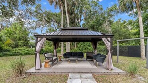 A covered outdoor seating area with a pergola, cushioned chairs, and a sofa.