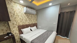 A neatly made bed with a grey and white striped blanket, a wooden headboard, and a wall-mounted air conditioner. - Hotel Fortune (Indore)