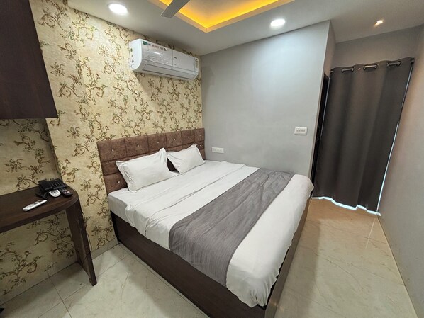 Uma cama bem arrumada com manta cinza e branca listrada, cabeceira de madeira e ar condicionado fixado na parede.