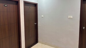 A hallway with three wooden doors, numbered 101, 102, and 103, and a light switch on the wall. - Hotel Fortune (Indore)