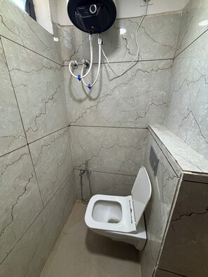A small, tiled bathroom with a toilet, a shower unit, and a wall-mounted control panel. - Hotel Fortune (Indore)