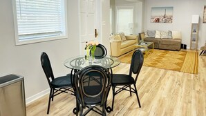 Un salon moderne avec une table à manger en verre, deux chaises noires, un canapé beige et un tapis à motifs.