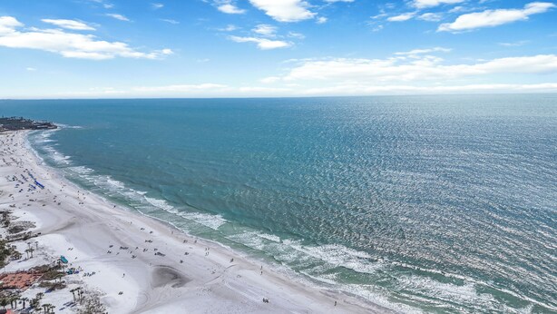 A beach with a long stretch of sand, a few umbrellas, and a few people.