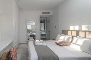 Quarto de hotel moderno com uma cama grande, um closet espaçoso, banheiro com chuveiro de vidro e vista para o exterior.