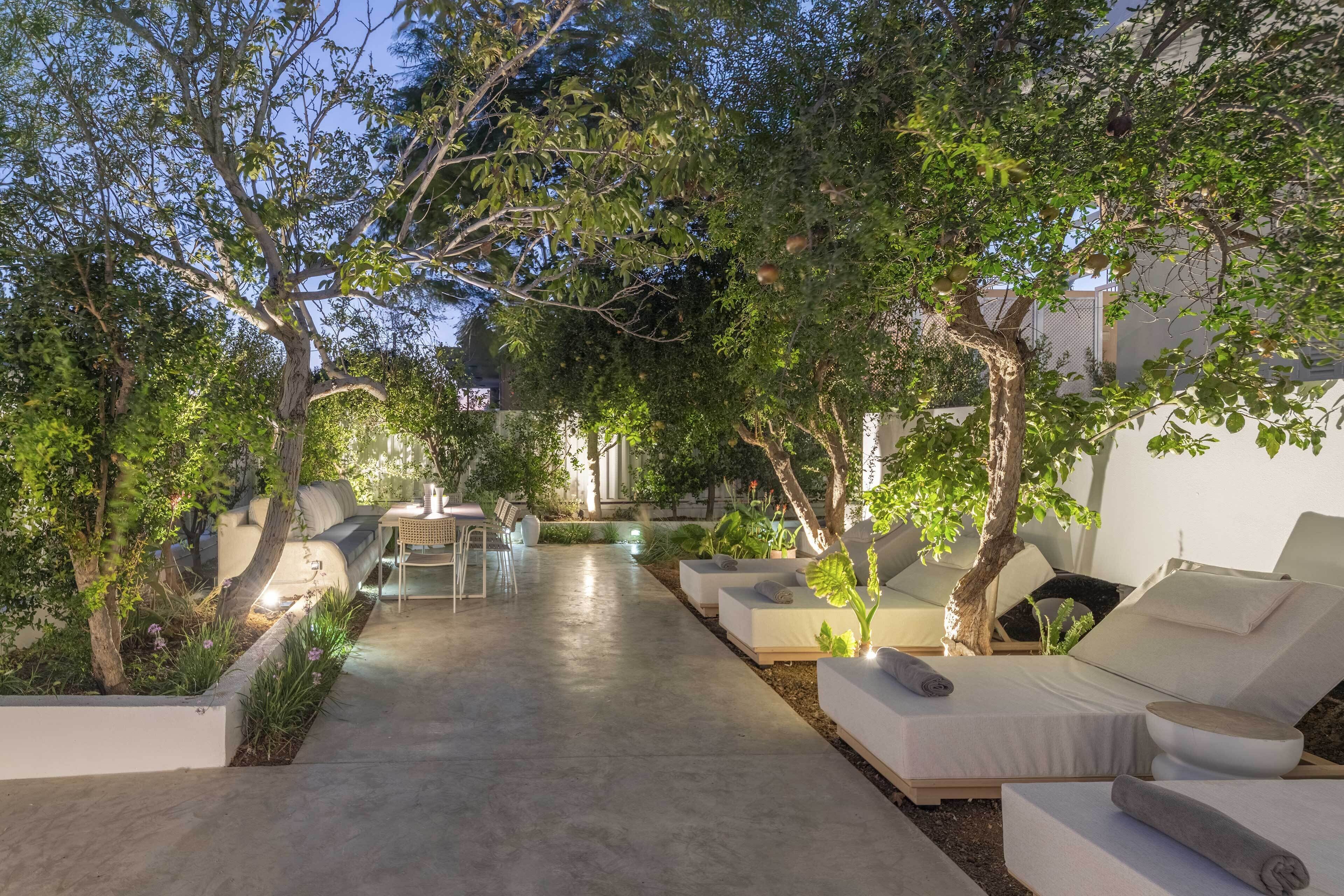 An outdoor lounge area with multiple seating options, including sofas and chairs, surrounded by trees and plants.