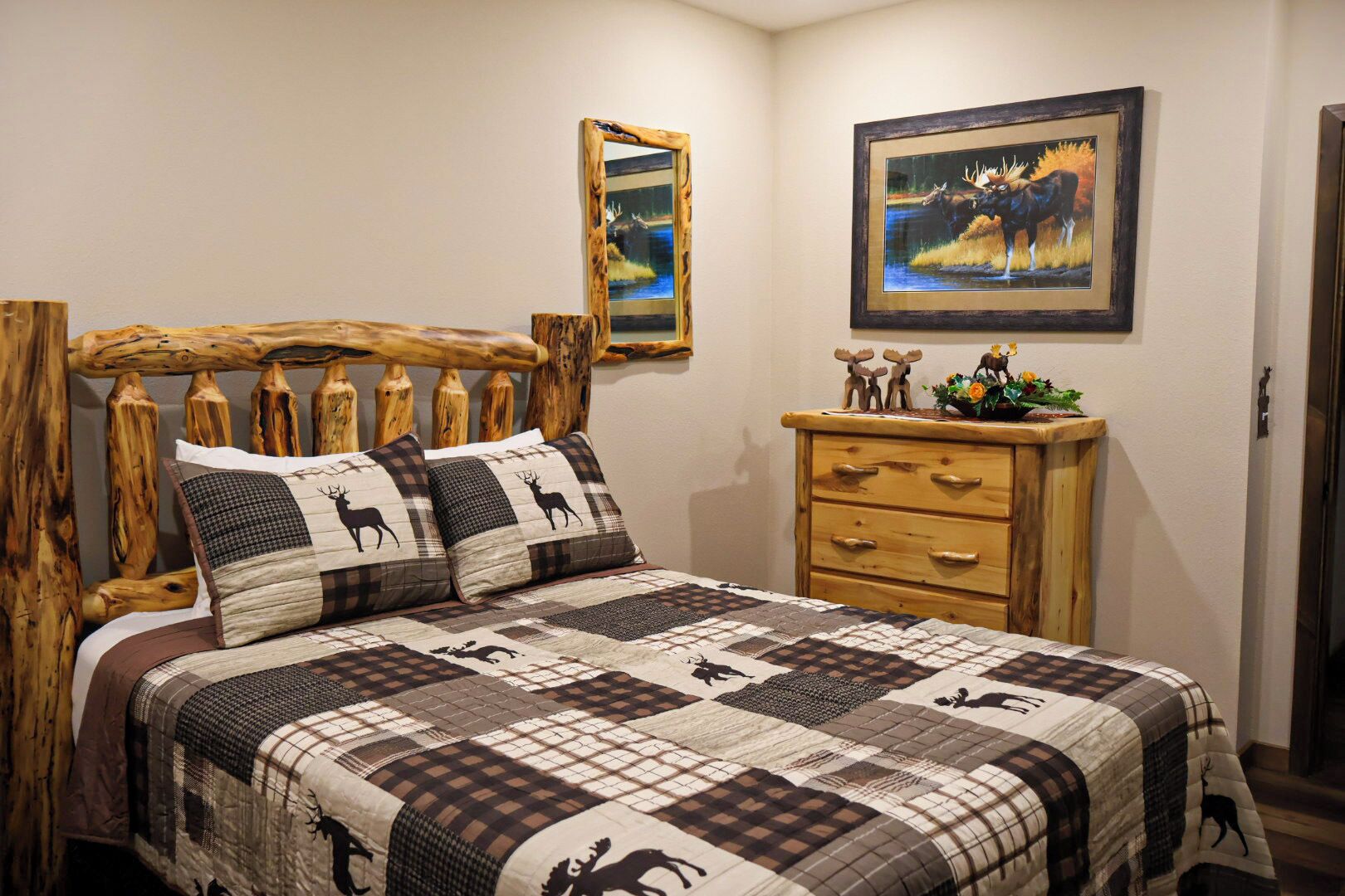 Quarto com cabeceira de madeira, colcha acolchoada, cómoda de madeira e quadro com uma imagem de alce.
