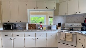 Una cocina con armarios blancos, microondas, tostadora, hervidor de agua y cafetera.