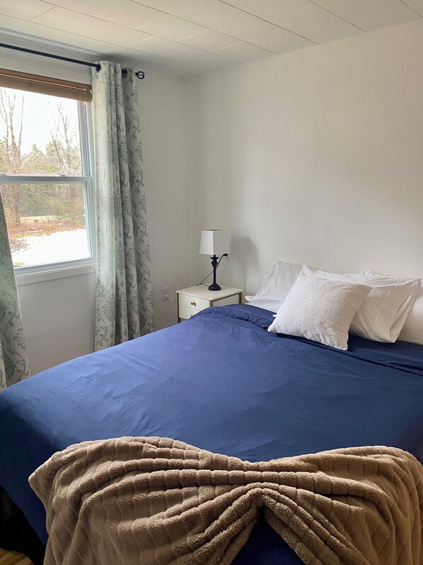 Une chambre à coucher avec un lit, une table de chevet, une lampe et une fenêtre avec des rideaux.