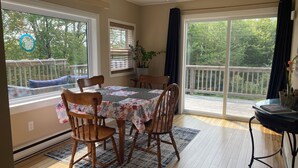 Un comedor con mesa y sillas, ventilador de techo y ventanas amplias con vistas a una terraza y árboles.