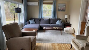 Una sala de estar con un sofá gris, dos sillones, una mesa de centro de madera y un tapete gris.